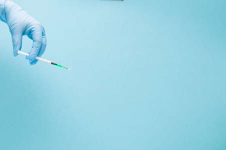 female hand in a blue rubber medical glove holding an insulin syringe with green medicine inside on a blue background copy space, treatment and health care concept, diabetes conceptの写真素材