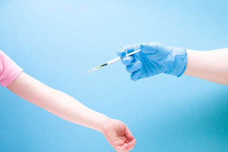 a female hand in a blue rubber medical glove injects a little girl with an insulin syringe on a blue background copy space, treatment and health care concept, child diabetes conceptの写真素材