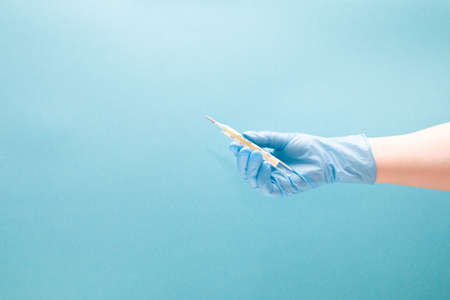 female hand in a blue disposable medical glove holds a mercury thermometer, blue background copy spaceの写真素材