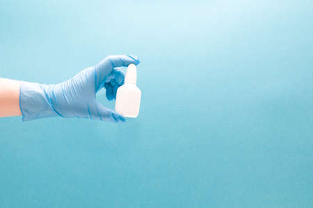 a female hand in a blue disposable medical glove holds a white plastic bottle with drops for the nose, blue background copy space, nasal drops, medicine for the noseの写真素材