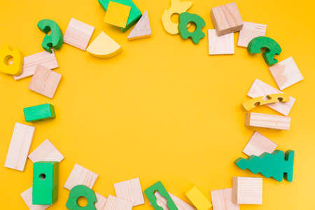 frame made of wooden details of the constructor and various wooden figures, green, yellow and natural parts for construction, natural materials Montessori concept, yellow background, top view, copy spaceの写真素材