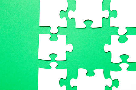 unfinished puzzle made of white cardboard on a green background and one unsuitable part from another...