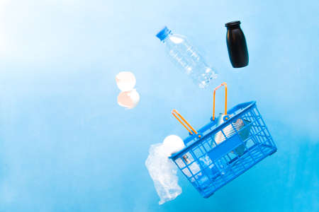 recycling trash flies with a shopping basket, blue background, conscious purchase concept, waste recycling, eco friendly lifestyle, copy spaceの写真素材