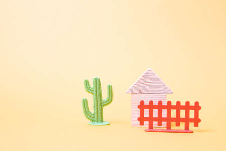 wooden toy house from the constructor for children, brown fence and green cactus toy on a yellow background copy space, life in the desert conceptの写真素材