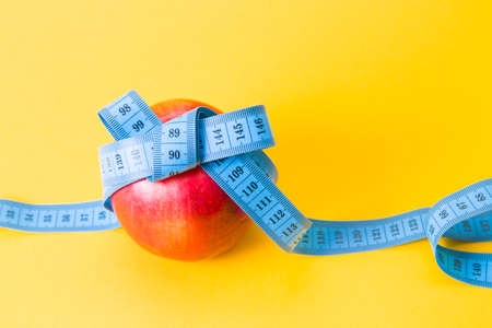 red apple tied with a blue measuring tape with a bow, copy space, yellow background, diet and weight...