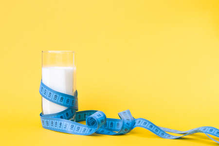 glass of milk and blue measuring tape on a yellow background, copy space, diet and milk products...