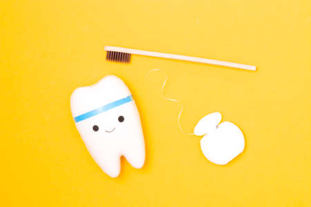 tooth model, dental floss and bamboo toothbrush on yellow background, happy tooth, white healthy tooth, copy space, oral care conceptの写真素材