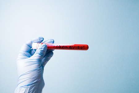 hand in blue medical disposable rubber gloves holds a test tube with red blood, inscription coronavirus on a test tube, blue background copy space, close-upの写真素材