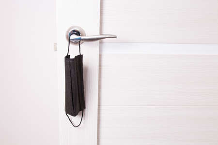black medical protective mask hanging on a doorknob, quarantine concept, coronavirus mirovach...