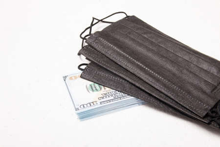 black medical protective masks and a stack of 100 dollar bills on a white background, copy space,...