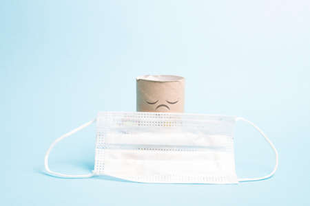 a toilet paper sleeve with a painted sad face and a protective white mask for children on a blue...