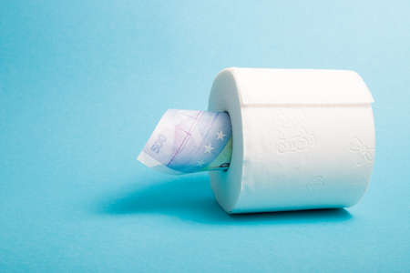 a roll of white toilet paper and several notes worth 500 euros, money in a roll of toilet paper, blue background copy spaceの写真素材