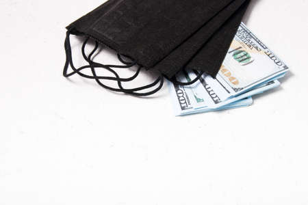 black medical protective masks and a stack of 100 dollar bills on a white background, copy space,...
