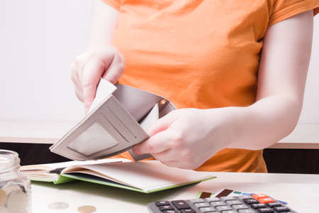 woman holds an empty wallet, copy space, coins, bank cards on the table and in a glass jar,...