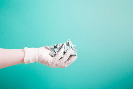 hand in a rubber white medical disposable glove holds crumpled dollar bills on a green background...