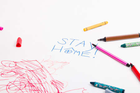 inscription on white paper stay home, felt-tip pens and wax crayons lie on drawing paper, child's drawing, activities with the child during quarantine, development of childrenの写真素材