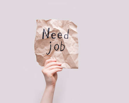 female hand holds a crumpled scrap of brown wrapping paper with the inscription need job, unemployment concept, light background, copy spaceの写真素材