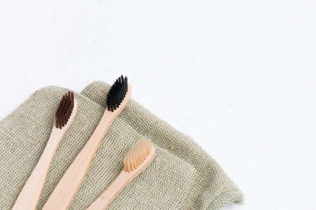 three bamboo toothbrushes on a coarse green natural fabric, white background copy space, top viewの写真素材