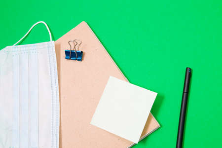 notepad with recycled cardboard cover and medical protective mask on a green background, copy space,...