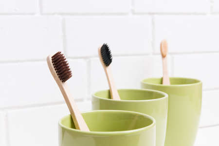 three toothbrushes in three different green cups on a white background, bamboo toothbrushes, social distance concept, copy space, eco friendly lifestyleの写真素材