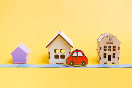 several models of houses on a yellow background, measured blue tape for measuring distance, red car...