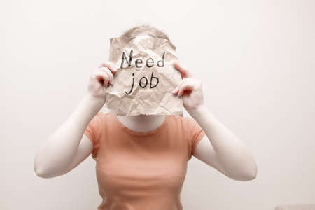 woman in orange foolfolk holds a piece of crumpled brown wrapping paper with the inscription need job, light background, copy space, unemployment concept, crisis 2020, no face trendの写真素材