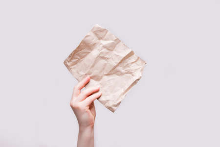 women hand holds a piece of brown wrapping paper, light background, copy spaceの写真素材