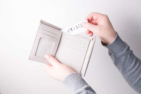 a woman gives a paper with the inscription crisis, copy space, a beige leather wallet and a small...