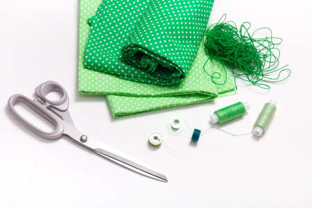 green polka dot fabrics, scissors and spools of thread on a white background, lace tangle and accessories for sewingの写真素材