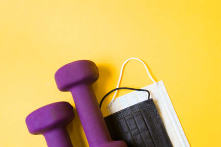purple dumbbells and medical protective masks of different colors on a yellow background. top view doing sports at home, healthy lifestyle conceptの写真素材