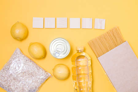 wooden squares for inscription donate or words of 6 letters, products for charity, yellow background, spaghetti, butter, oatmeal, lemons and a can of canned foodの写真素材