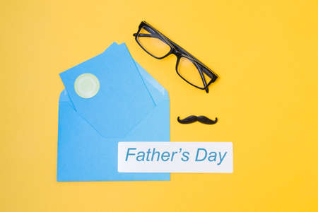 glasses, mustache, blue envelope and postcard on a yellow background, top view, copy space, father's day conceptの写真素材