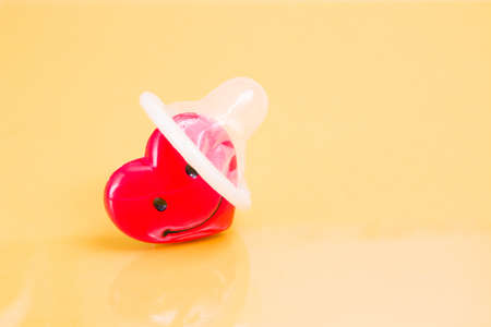 a condom is put on a heart, a happy red heart and a condom, yellow background, protected sex concept, sex for love between loversの写真素材