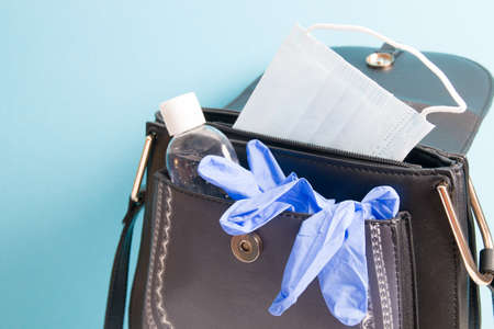 gel alcohol sanitizer, face mask and blue rubber disposable gloves in a handbag on a blue background, copy space, what to take when going out during a pandemicの写真素材