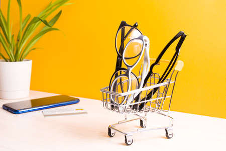 several pairs of different glasses for vision correction in a small shopping cart on the table,...