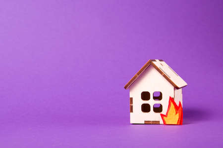 burning wooden model of a house, fire cut out of felt, purple background copy space, insurance and protection of real estate concept, arson of a house, flammable materialの写真素材