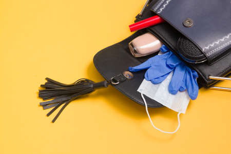 ladies bag with cosmetics and virus protection during a pandemic, black face mask and blue rubber disposable gloves on a yellow background, copy space top viewの写真素材