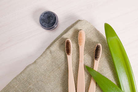 bamboo toothbrushes on natural coarse cloth on a wooden table, homemade charcoal toothpaste in a small glass jar, leaves long plants, eco friendly life style conceptの写真素材