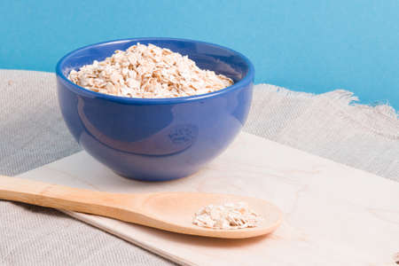oatmeal in a blue bowl and a wooden sick spoon on the table, blue background, copy space, cutting...