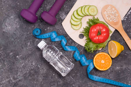 bottle of water, dumbbells, measuring tape, diet food on a black background, copy space, vegetables,...