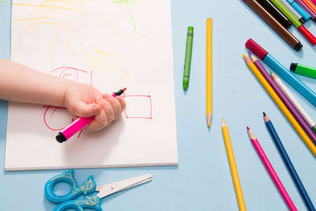 a small child painstakingly draws with a pink felt-tip pen in an album, copy space, top view, blue...