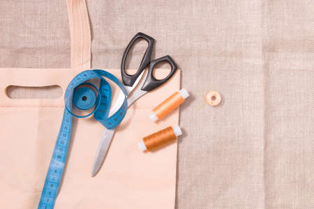 eco bag, scissors, measuring tape and several spools of thread on linen fabric, top view, copy location. environmental materials, flax textureの写真素材
