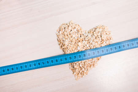 heart-shaped oatmeal and blue measuring tape on a wooden table, copy space, top viewの写真素材
