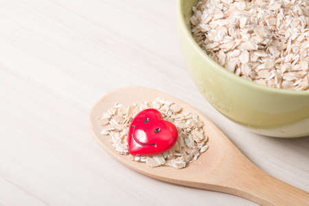 oatmeal in a green bowl and a wooden big spoon with oatmeal and a small red happy heart on a wooden...