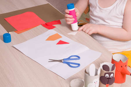 a small child smears paper with glue, children's safe scissors and colored paper on the table, what to do with the child at home, children's hands make an applicationの写真素材
