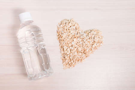 heart-shaped oatmeal and a small transparent bottle of water on a wooden table, copy space, top viewの写真素材