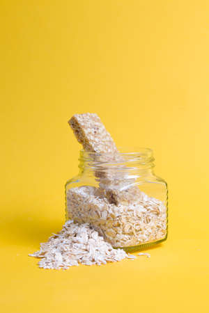 glass jar with oatmeal and several protein bars for a snack on a yellow background, sprinkled oatmeal, copy space, healthy proper nutrition conceptの写真素材