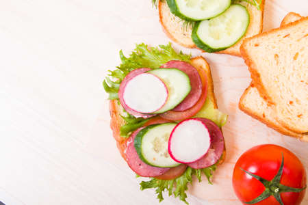 a sandwich of vegetables and diet sausage on a wooden cutting board, wooden table, bread and vegetables in the background, healthy breakfast concept, copy spaceの写真素材