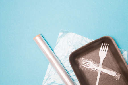 various disposable plastic packaging on a blue background, a food tray, a roll of plastic tape and a bag for freezing food, a disposable fork and a drinking tube, environmental pollution conceptの写真素材