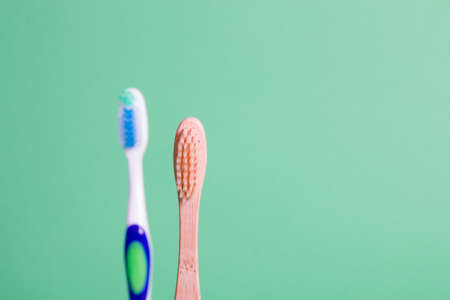 bamboo and plastic toothbrushes on a green background, eco friendly lifestyle concept, plastic...
